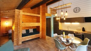 L’intérieur chaleureux d’un chalet en bois comprend un espace de vie avec un lit en mezzanine, un coin repas avec une table et des chaises, et une cuisine équipée d’appareils électroménagers modernes.