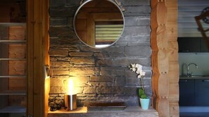 Une cheminée en pierre surmontée d’un grand miroir rond, une petite table avec une lampe et une plante en pot.