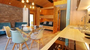 Un intérieur chaleureux, aménagé dans le style d’un chalet, comprenant un coin repas, une chambre en mezzanine et une cuisine.