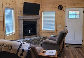 Cozy cabin interior with a fireplace, flat-screen TV, and comfortable seating area.