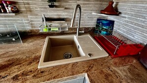 Een keuken met een spoelbak, een afdruiprek en een rek voor kruiden.