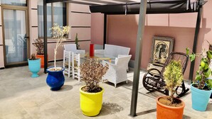 Een overdekt terrasgedeelte met buitenmeubilair, potplanten en een pergola.