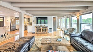 A spacious living area with a wooden ceiling, a leather sofa, a coffee table, and a view of the kitchen and dining area through large windows. - Stunning Enfield Home w/ Deck & Boat Dock! (Enfield)