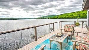 A wooden deck with a table and chairs overlooking a lake, with a view of green hills in the distance. - Stunning Enfield Home w/ Deck & Boat Dock! (Enfield)