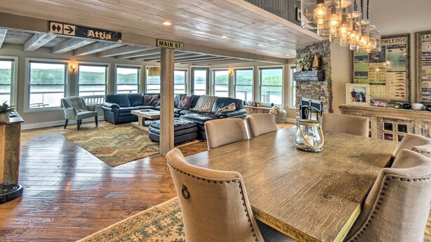 A spacious living area with a large wooden dining table, comfortable seating, and large windows offering views of the outdoors. - Stunning Enfield Home w/ Deck & Boat Dock! (Enfield)