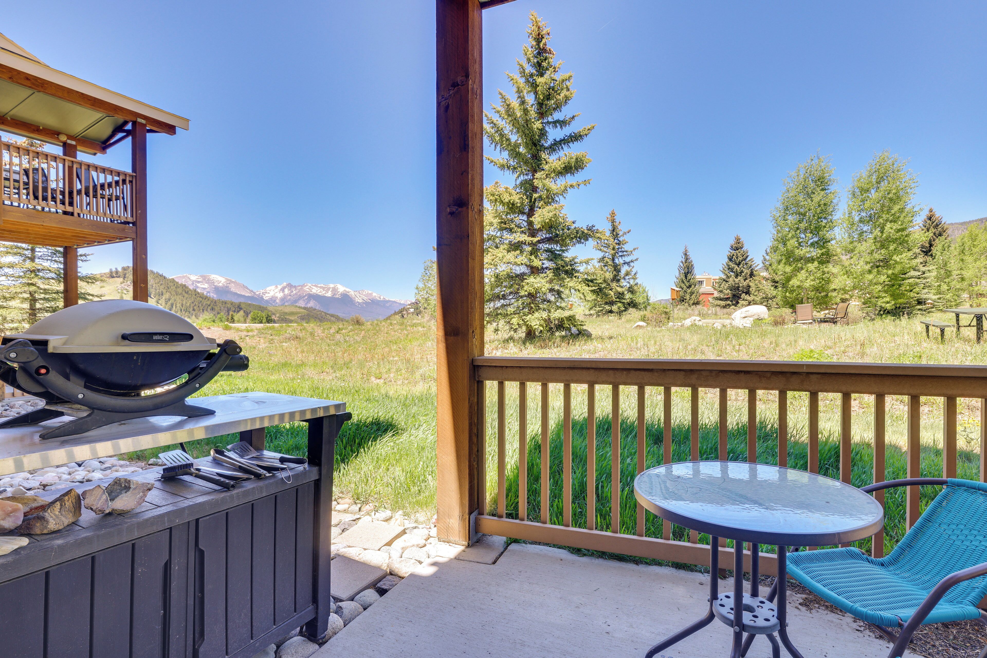 A patio with a grill, outdoor table, and chairs, overlooking a mountainous landscape.