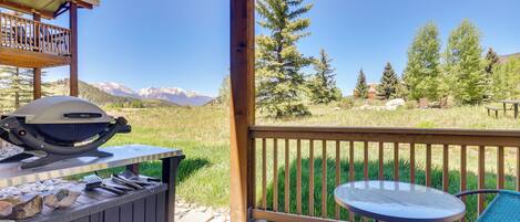 A patio with a grill, outdoor table, and chairs, overlooking a mountainous landscape.