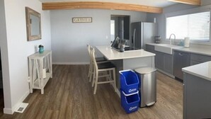Une cuisine moderne dotée d’un îlot central, de poutres en bois au plafond et d’un panneau mural portant l’inscription « GATHER ».