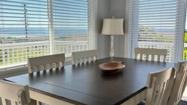 Un coin repas avec une table en bois foncé, des chaises blanches dotées de coussins noirs et une lampe de table blanche.