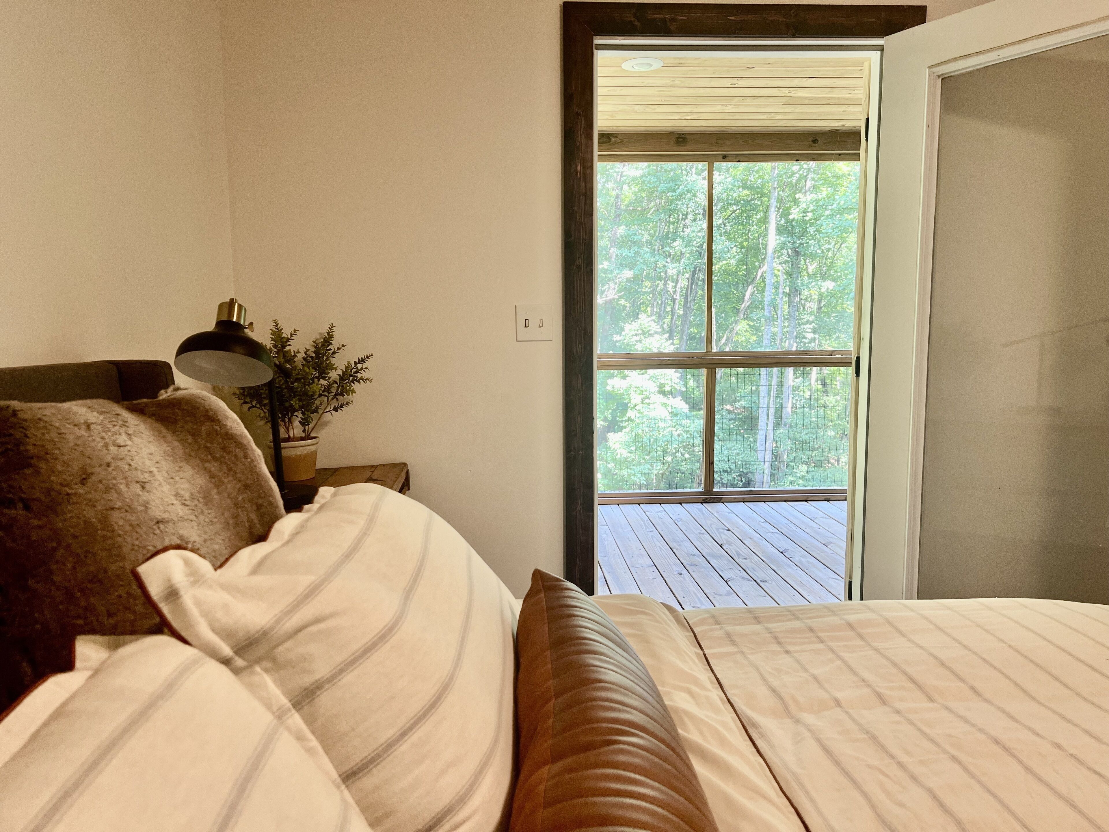 A bedroom with a bed, a nightstand, a lamp, and a window with a view of trees.