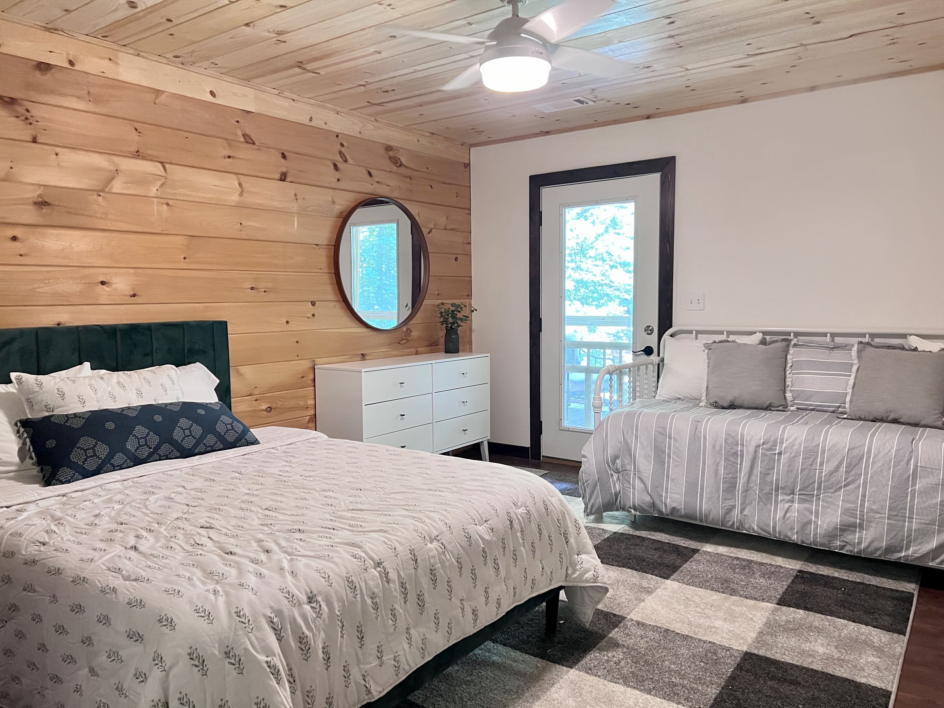 Quarto com duas camas, cômoda, espelho e ventilador de teto.