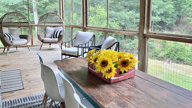 A wooden deck with wicker chairs and a table with sunflowers. - NEW Cabin by Blue Ridge Lake, Swing Bed, Firepit, Double Porches (Morganton)