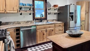 A modern kitchen with wooden cabinets, a stainless steel refrigerator, and a granite countertop. - NEW Cabin by Blue Ridge Lake, Swing Bed, Firepit, Double Porches (Morganton)