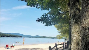 A beach with a wooden fence, a sandy shore, and people swimming. - NEW Cabin by Blue Ridge Lake, Swing Bed, Firepit, Double Porches (Morganton)