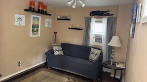 A living room with a sofa, a rug, wall art, a ceiling fan, and a window with curtains. - Walk to Beach  2BR Near Dining & Shopping (Rocky Point)