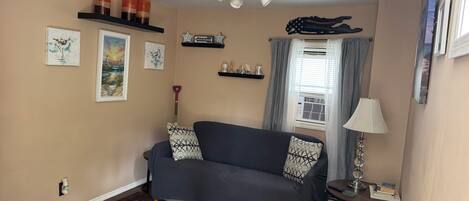 A living room with a sofa, a rug, wall art, a ceiling fan, and a window with curtains.