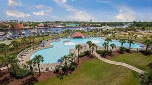 A large, multi-pond pool area with lounge chairs and umbrellas, surrounded by palm trees and a marina in the background.