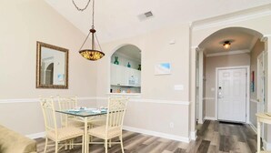 A dining area with a table and chairs, a hanging light fixture, and a mirror on the wall.