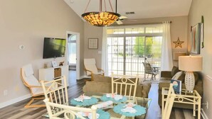 A spacious living room with a glass coffee table, white chairs, a sofa, and a TV mounted on the wall.