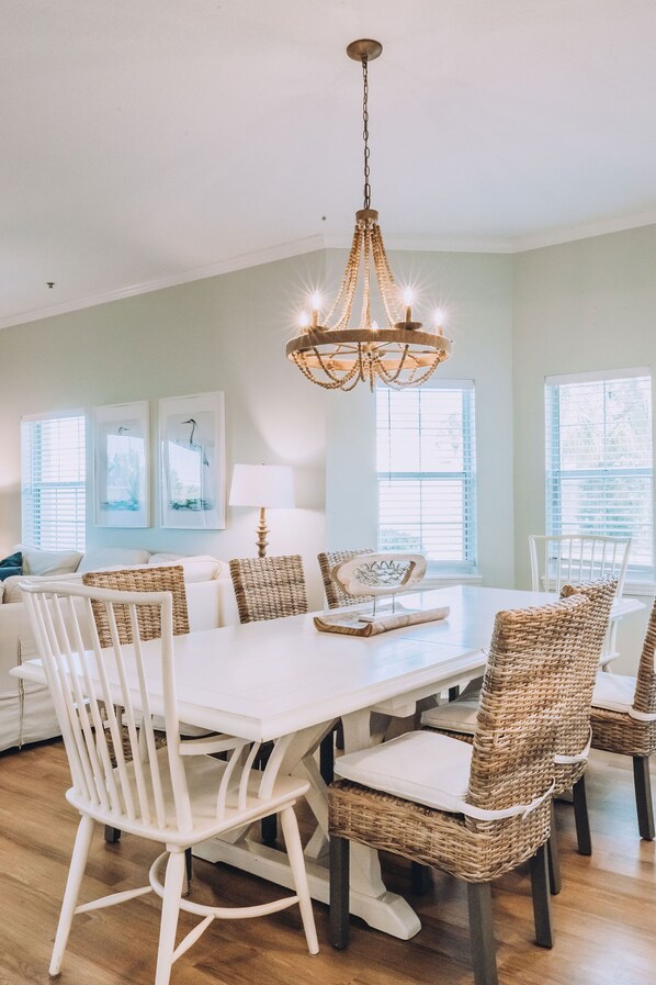 Un coin repas avec une table blanche, des chaises en osier et un lustre.