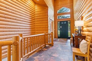 A log cabin interior with a wooden staircase, a dining area with a table and chairs, and a door leading outside.
