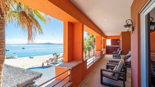 Een balkon met uitzicht op een strand en de oceaan, voorzien van lounge stoelen en een klein tafeltje.