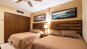 Hotelkamer met twee bedden, een houten hoofdeinde, een plafondventilator en kunst aan de muur.
