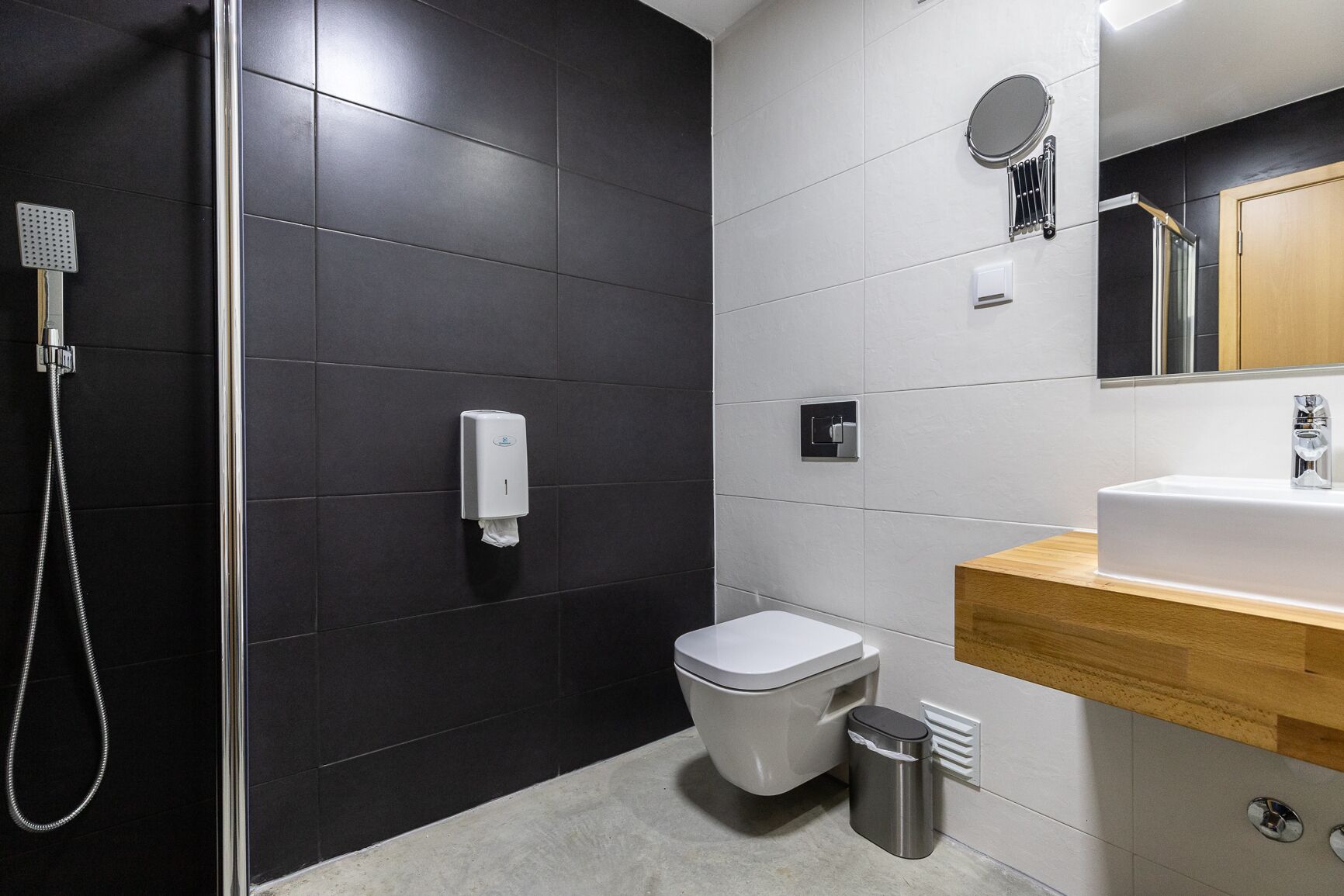 Un baño moderno con ducha de vidrio, inodoro, lavamanos con encimera de madera y espejo.