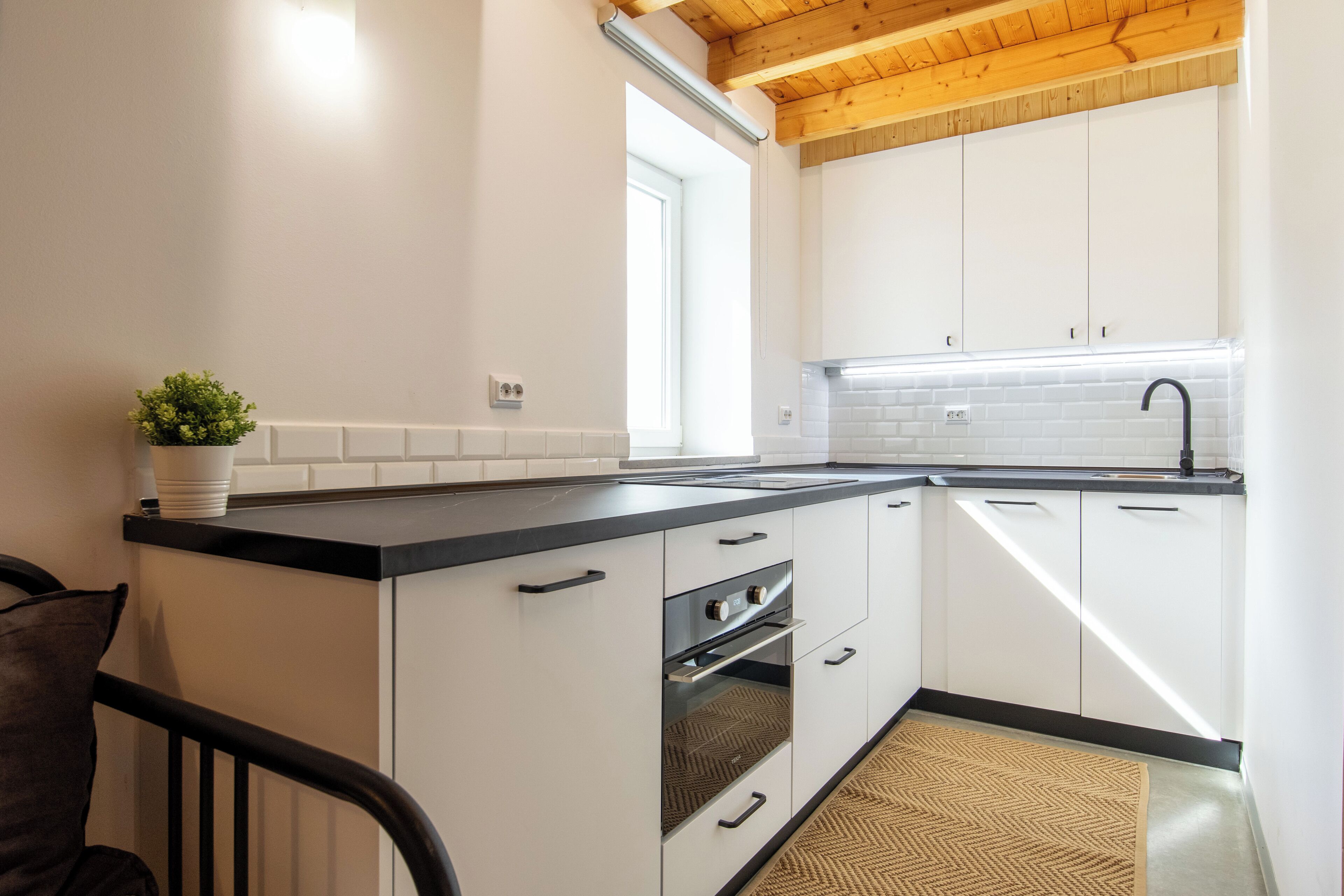 A modern kitchen with white cabinets, a black countertop, and a wooden ceiling.