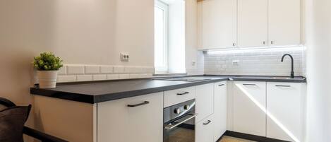 A modern kitchen with white cabinets, a black countertop, and a wooden ceiling.