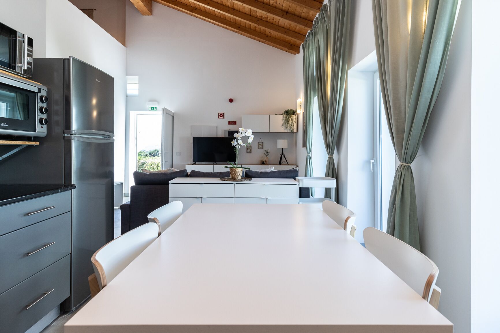 Une cuisine moderne dotée d’un grand îlot central, d’appareils électroménagers intégrés et d’un coin repas avec une table et des chaises blanches.