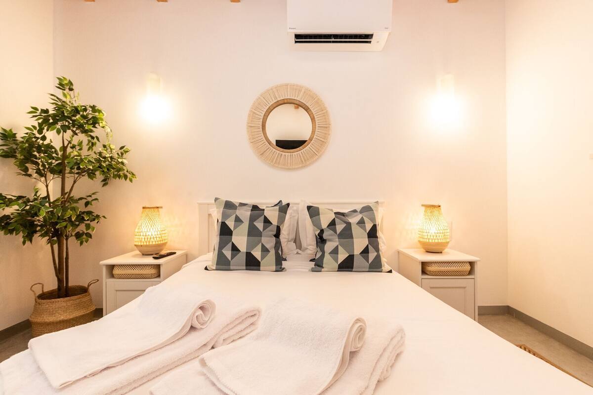 A neatly made bed with towels, a round mirror, bedside lamps, and a potted plant in a hotel room.