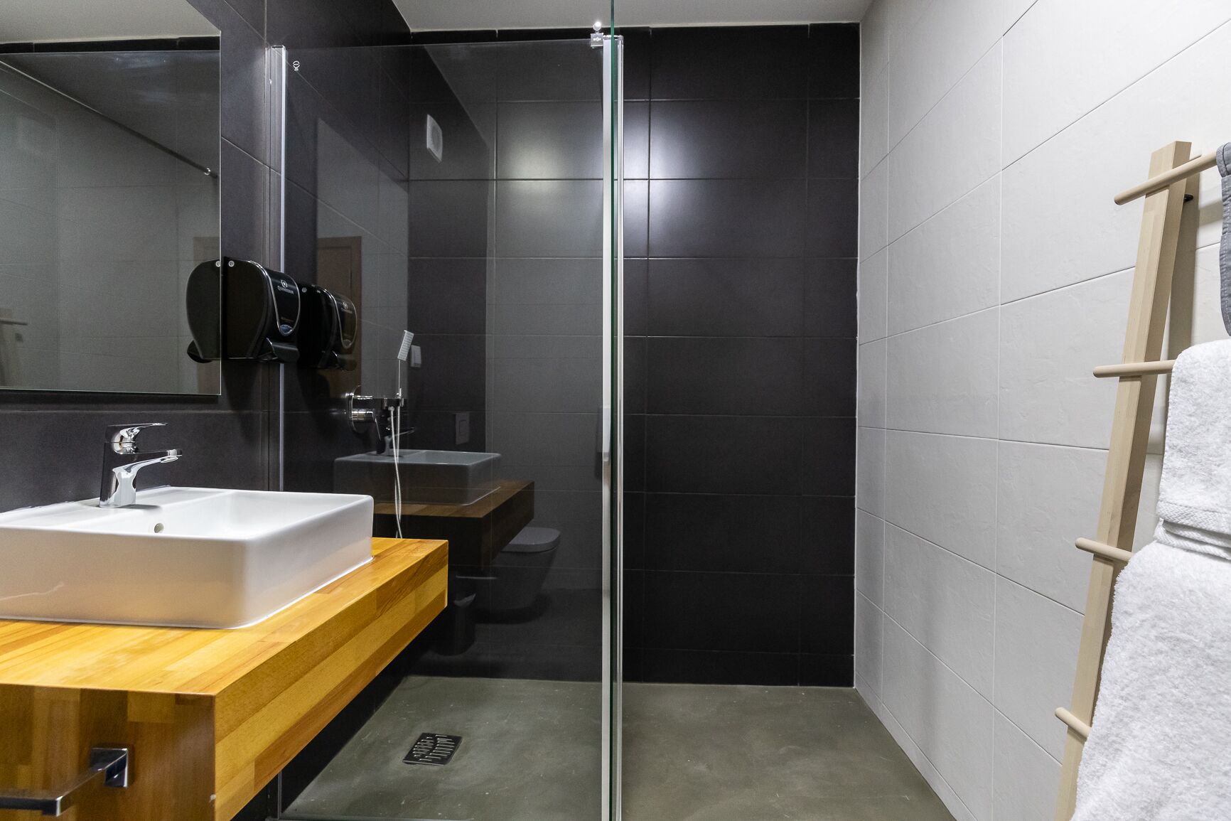 Un baño moderno con cabina de ducha de vidrio, tocador de madera y lavamanos blanco.