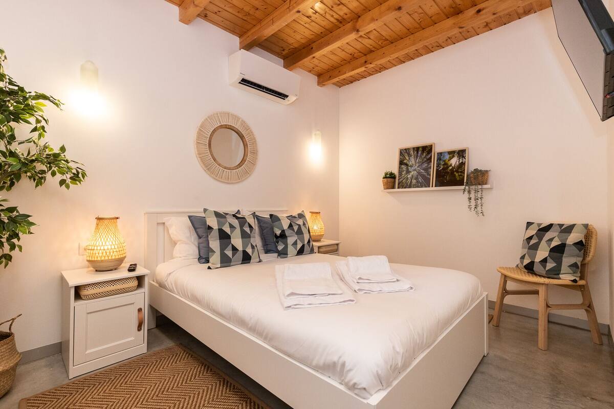 A bedroom with a bed, bedside tables, a mirror, a wall-mounted air conditioner, and a chair.