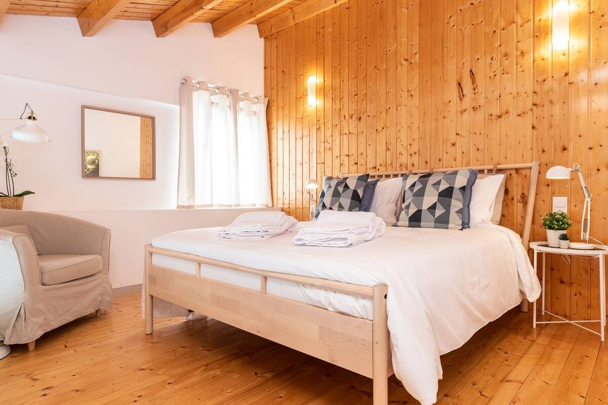 A wooden-paneled room with a bed, a chair, a lamp, and a mirror.