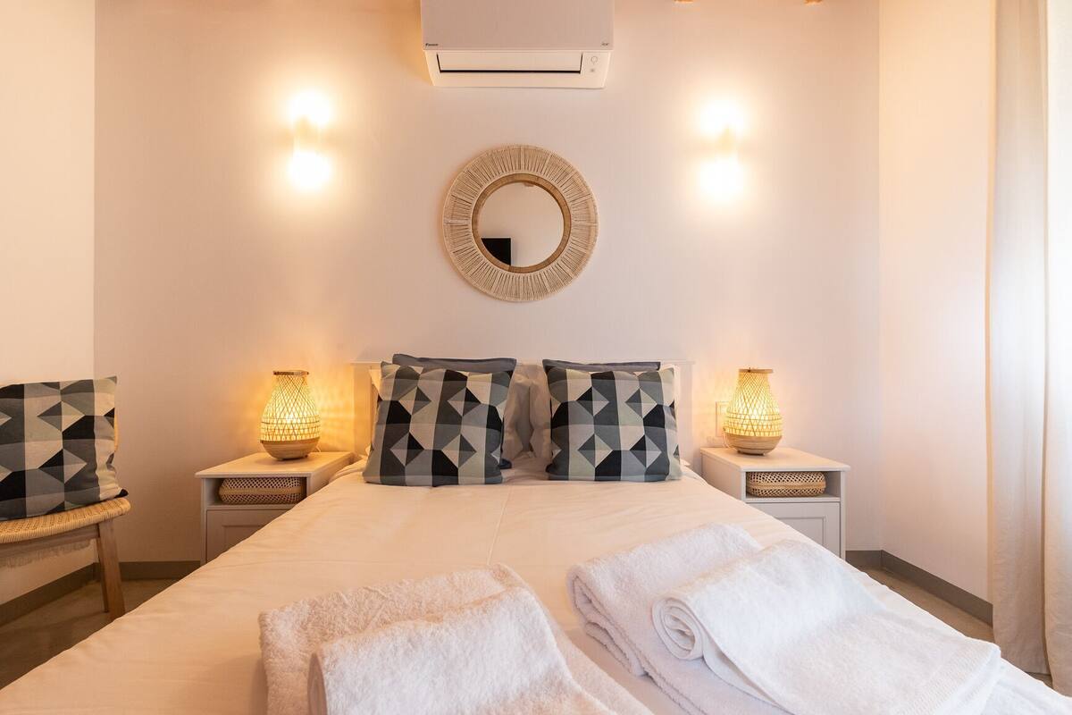 A hotel room with a bed, two nightstands with lamps, a round mirror, and a chair.