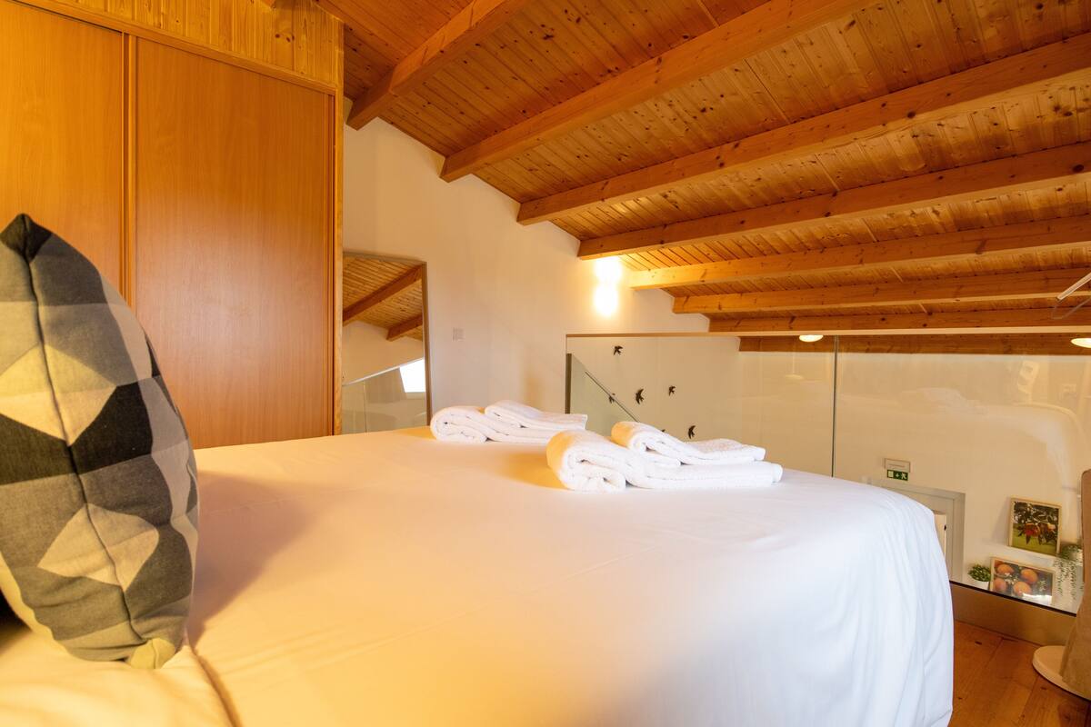 A hotel room with a wooden ceiling, a bed with white linens, and a mirror on the wall.