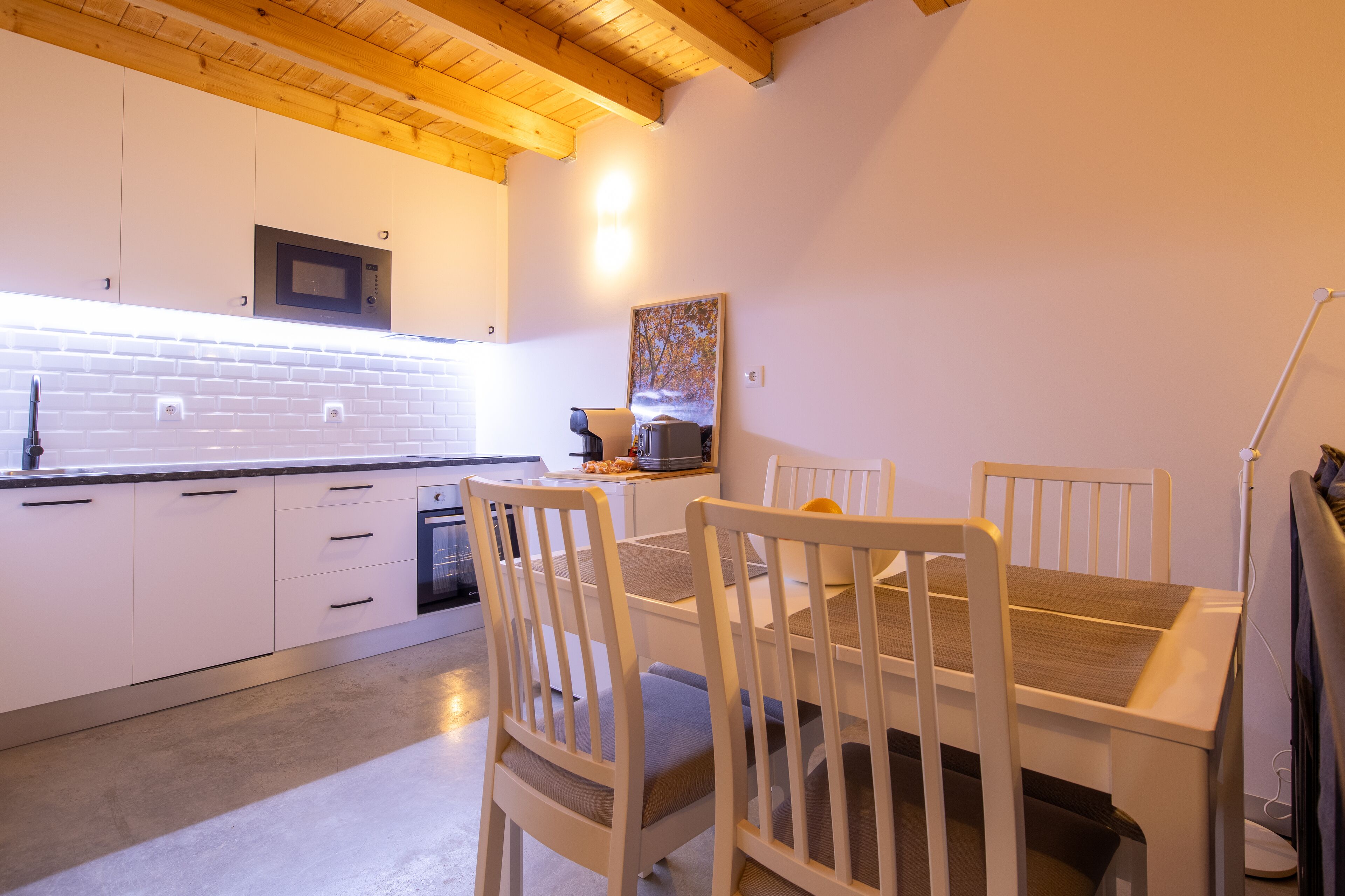 A modern kitchen with white cabinets, a microwave, and a dining area with white chairs and a table.