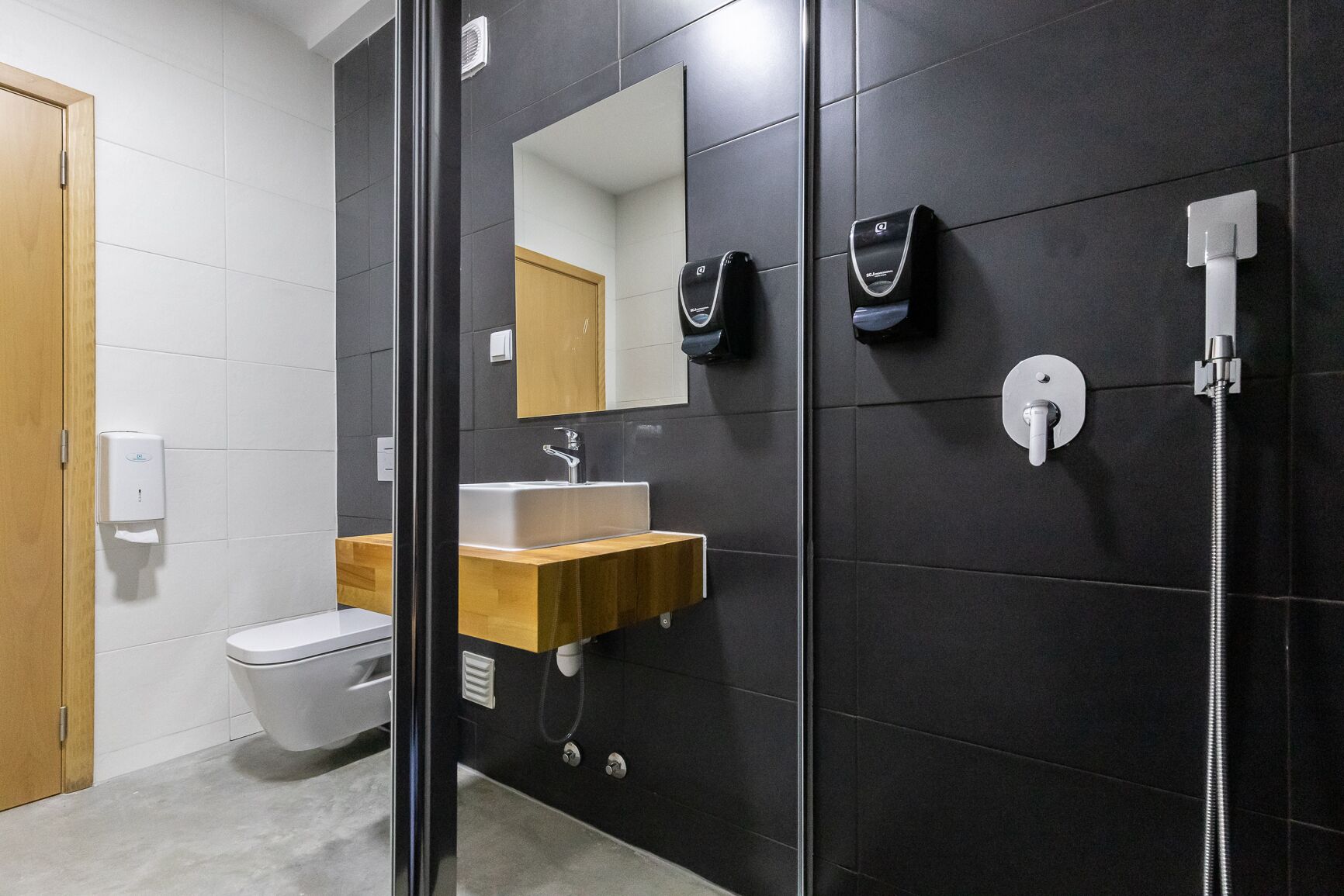 Un baño moderno con separador de vidrio, tocador de madera, inodoro blanco, espejo y ducha con cabezal de ducha manual.
