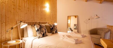 A cozy bedroom with a large bed, two bedside lamps, a chair, and a wooden ceiling.