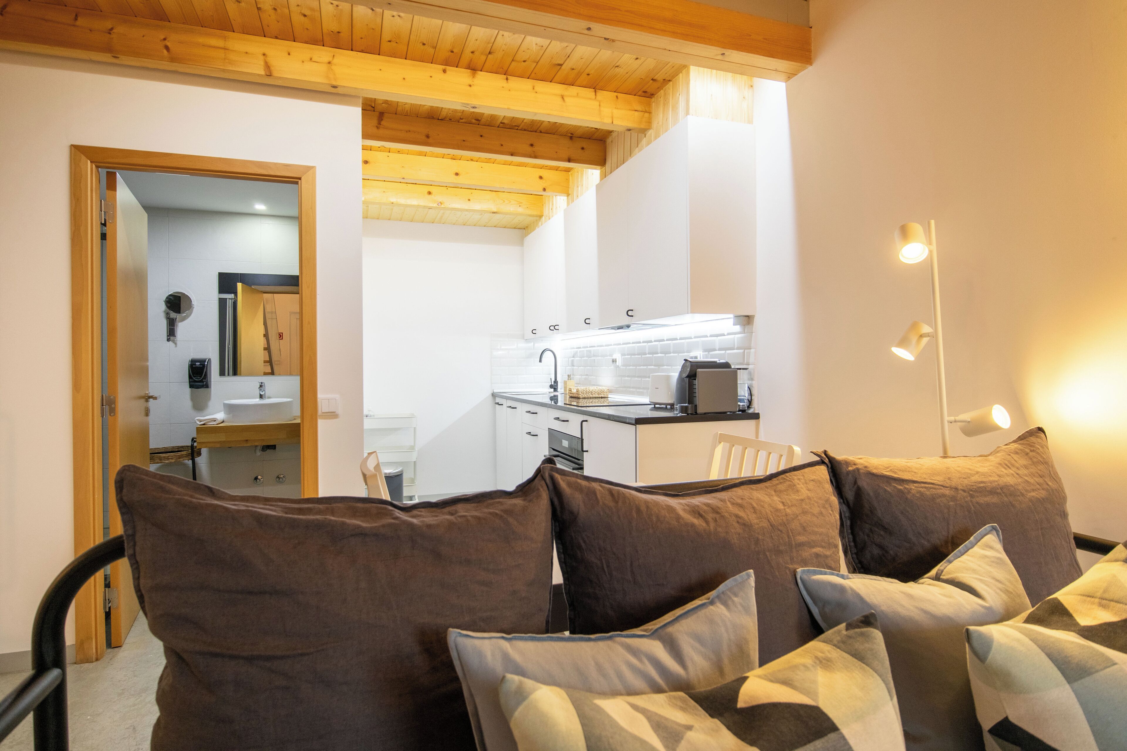 Un interno moderno con soffitto in legno, angolo cottura e zona salotto con cuscini.