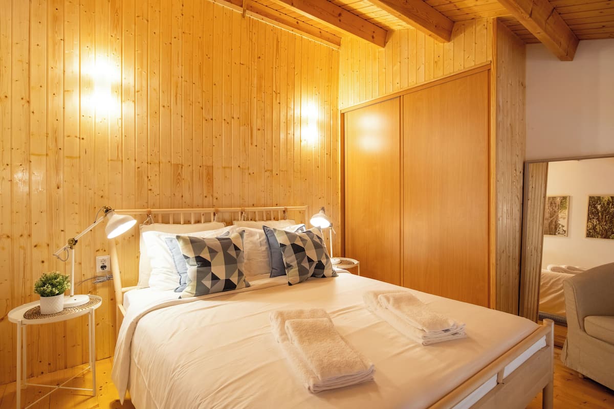 A wooden-paneled room with a bed, bedside lamps, and a small table with a plant.