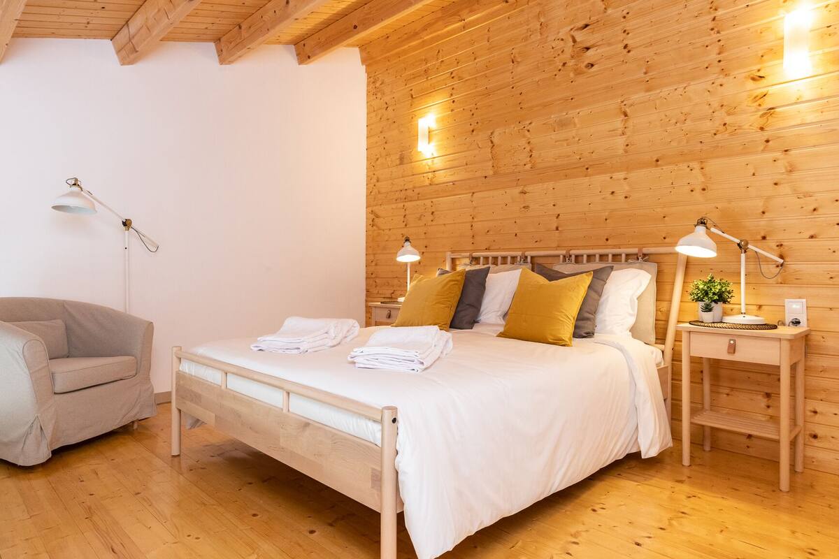 A wooden-paneled room with a bed, bedside tables, a lamp, and a chair.