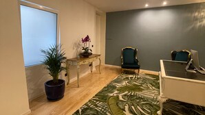 A modern living room with a wooden floor, a large window, a desk with a plant, a blue armchair, and a white sofa. - Pier House Accommodation (Funchal)