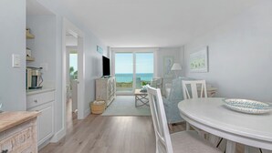 A modern kitchen with a view of the sea, a dining area with a white table and chairs, and a cozy seating area with a lamp. - Beachcrest Gulf-Front Private Beach- Chair & umbrella service -March-Oct (Santa Rosa Beach)