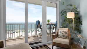 Ein Balkon mit Blick auf Strand und Meer, ein Korbstuhl, eine Stehlampe und ein Blumentopf.