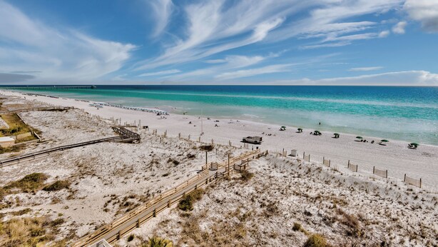 Ein Strand mit einer Holzpromenade, feinem Sand und einem Pier in der Ferne.