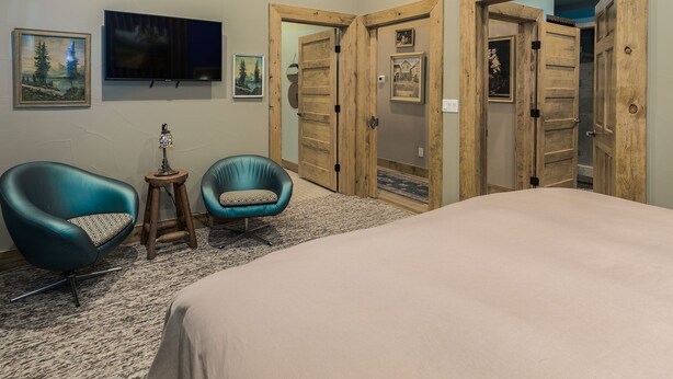 Een slaapkamer met een bed, twee stoelen, een televisie en houten deuren.