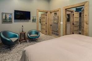 A bedroom with a bed, two chairs, a TV, and wooden doors.