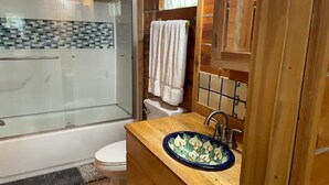 Un bagno con cabina doccia in vetro, un water bianco, un mobiletto in legno con lavabo in ceramica blu e uno schienale rivestito in piastrelle.